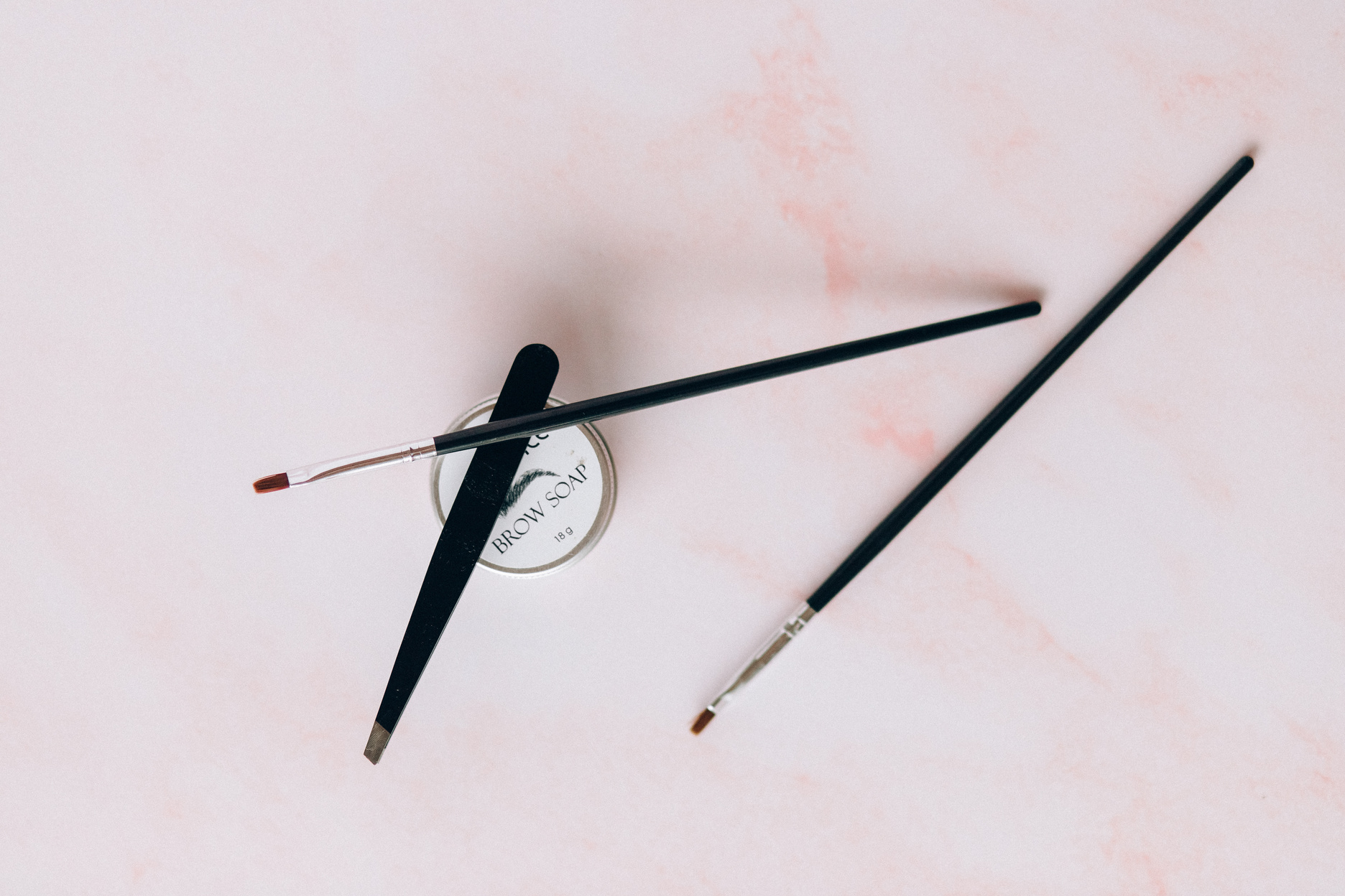 Tweezer, Make-up Brushes and Brow Soap on a Pink Surface